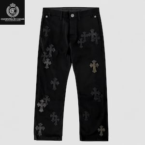 May include: Black pants featuring a series of dark, textured cross-shaped patches scattered across the front. The trousers include a button closure at the waist, belt loops, and silver-toned metal hardware on the pockets and fly area.