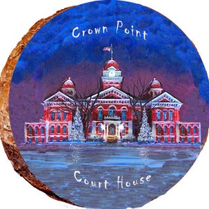 May include: A painting of a red brick courthouse with a white dome and a clock tower. The courthouse is surrounded by trees and snow. The painting is on a round wooden surface with the words "Crown Point Court House" written on it.