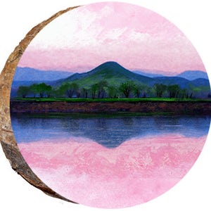 May include: A round wooden slice featuring a landscape painting. The artwork depicts a green mountain, trees, and a body of water reflecting the sky. The sky is a blend of pink and blue hues.