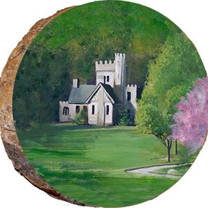 May include: A painting on a wood slice depicting a white stone house with a tower, surrounded by green trees and a pink flowering tree. The house has a green roof and white trim. The scene is set in a grassy field with a winding path leading to the house.