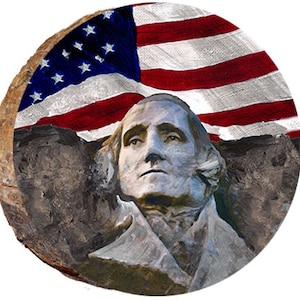 May include: A close-up of a stone carving of a man's face, with the American flag draped over the top. The carving is weathered and has a rough texture. The flag is red, white, and blue.