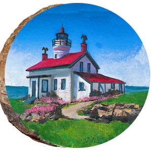 May include: A round wooden slice featuring a painting of a white lighthouse with a red roof and a tall, white tower. The lighthouse sits on a green grassy hill with pink flowers, under a blue sky.