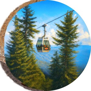 May include: A round wooden coaster featuring a painting of a ski lift car suspended by a cable between two tall green pine trees. The background shows a blue sky and distant mountains.