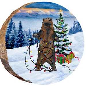 May include: A brown bear tangled in Christmas lights stands in front of a decorated Christmas tree in a snowy forest setting.