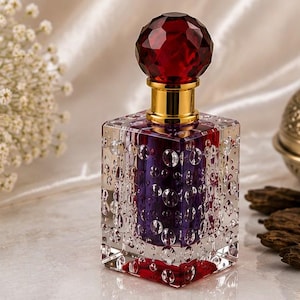 May include: A square glass perfume bottle with a clear exterior featuring a bubble-like texture. The inner core is deep purple, and the bottle is topped with a faceted, round, dark red stopper and a gold-colored neck collar.