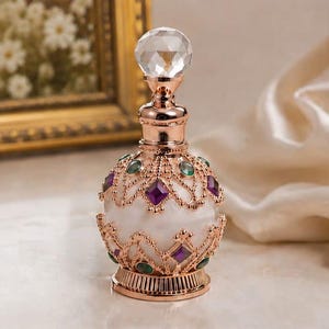 May include: A decorative perfume bottle featuring a white opaque glass body encased in a rose gold metal filigree overlay. The bottle is adorned with inset purple diamond-shaped and green oval-shaped stones, topped with a clear faceted crystal stopper.