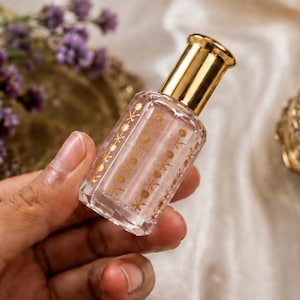 May include: A small, rectangular glass perfume bottle with a gold-colored cap. The clear glass body features a repeating vertical pattern of gold-colored floral motifs. The bottle has a smooth, polished finish and a metallic gold-toned neck and lid.