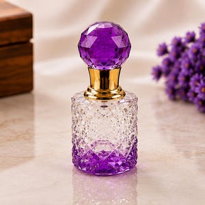 May include: A clear and purple ombre glass perfume bottle with a diamond-cut textured pattern. The bottle features a gold-colored metal neck and a large, spherical, faceted purple glass stopper that sits securely on top of the bottle opening.