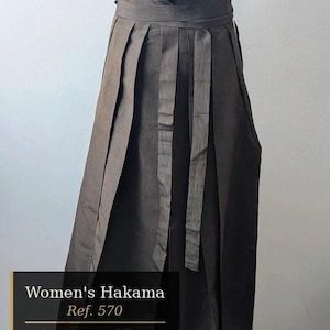 Peut inclure: Un hakama plissé marron foncé avec une large ceinture et un système de nouage. Le vêtement présente des rayures verticales et une longueur de 84 cm. Le texte sur l'image indique : Women's Hakama, Ref. 570, Longueur: 84 cm, Taille: ajustable.