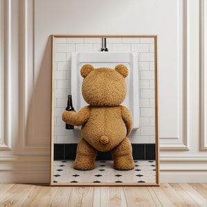 May include: A framed wall art print featuring a brown teddy bear standing at a white porcelain urinal. The bear is holding a dark brown glass beer bottle in its right hand. The background shows white subway tiles and a black and white tiled floor.
