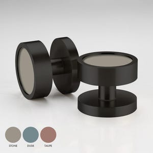 May include: Two black cabinet knobs with a round, flat top and a circular base. The top of the knob is a light grey colour.