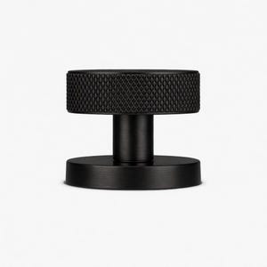 May include: A black, cylindrical door knob with a textured, diamond-patterned grip. The knob has a short, cylindrical stem connecting it to a circular base. The hardware is made of metal and is set against a white background.