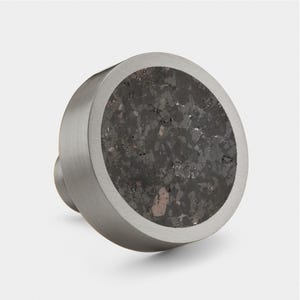 May include: A round, silver knob with a dark grey, speckled, concrete-like centre. The knob has a smooth, brushed finish.