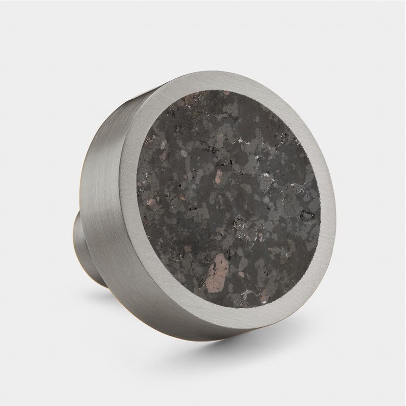 May include: A round, silver knob with a dark grey, speckled, concrete-like centre. The knob has a smooth, brushed finish.