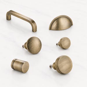 Peut inclure: Un ensemble de six pièces de quincaillerie pour armoires avec une finition en laiton antique brossé. Le lot comprend une poignée rectangulaire, une poignée coquille semi-circulaire, trois boutons circulaires de tailles variées et un bouton cylindrique.