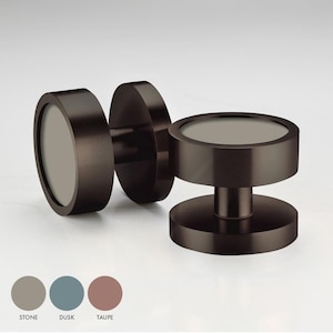 May include: Two round, dark bronze cabinet knobs with a slightly raised, circular, light grey centre. The knobs are shown against a white background.