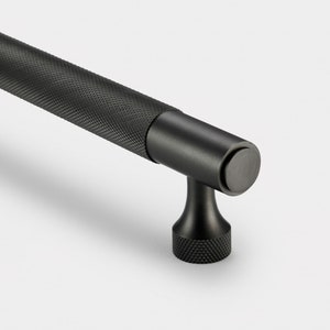May include: Black metal cabinet pull with a textured finish and a round knob. The pull is designed for use on cabinets and drawers.