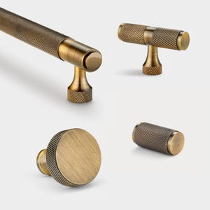 Może przedstawiać: Cztery antyczne mosiężne gałki i uchwyty do szafek z fakturowanym wykończeniem. Gałki i uchwyty mają różne kształty, w tym okrągłe, cylindryczne i w kształcie litery T.