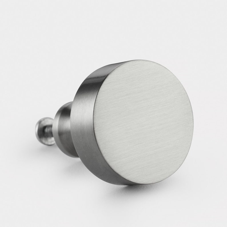 May include: A round, brushed nickel cabinet knob with a smooth, flat surface.