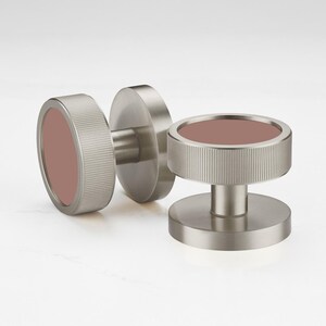 May include: Three brushed metal cabinet knobs with a circular design. Each knob features a ridged, cylindrical edge and a flat, circular center in a muted rose color. The knobs are designed for easy installation and add a modern touch to any cabinet.