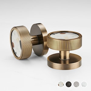 Puede incluir: Dos pomos de armario de color bronce con un diseño circular. Cada pomo presenta un borde texturizado y acanalado y una incrustación central con un patrón moteado de blanco, negro y marrón. Para muebles y decoración del hogar.