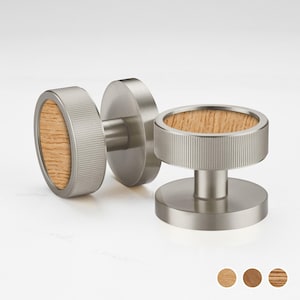 Puede incluir: Tres pomos de armario modernos con acabado metálico cepillado y centro de veta de madera. Los pomos tienen un diseño circular con borde estriado. La veta de la madera es marrón claro. Los pomos se muestran sobre un fondo blanco.