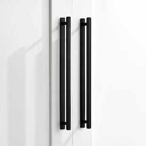 Peut inclure: Deux poignées de porte rectangulaires noires, chacune avec un bord légèrement arrondi, sont montées sur un mur blanc.