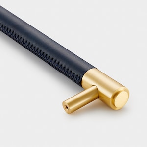 May include: A brass cabinet pull with a blue leather handle. The handle has a stitched edge and the pull has a T-shaped design.