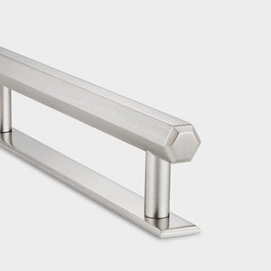 Pode incluir: Uma puxador de armário de níquel escovado com uma tampa hexagonal e uma base retangular.