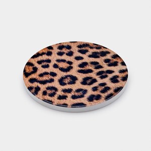 May include: A round, leopard print design with a white border. The design features a tan background with dark brown spots. The item is a circular shape, and the border is a solid white color.