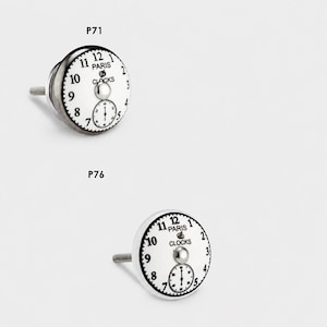 May include: Two round cabinet knobs labeled P71 and P76. Each knob features a white face with black clock numerals, the text PARIS CLOCKS, and a small sub-dial. A silver-toned metal post extends from the back of each knob for mounting purposes.