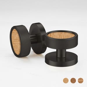 Pode incluir: Três puxadores de armário pretos com um centro de grão de madeira. Os puxadores têm uma forma cilíndrica com uma borda canelada. O grão da madeira é castanho claro. Os puxadores são exibidos em uma superfície branca.