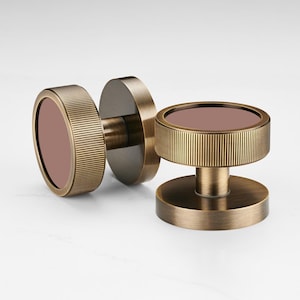 May include: Two antique brass cabinet knobs with a circular design. Each knob features a ridged, cylindrical outer ring and a flat, circular center in a muted rose color. The knobs are displayed against a white background.