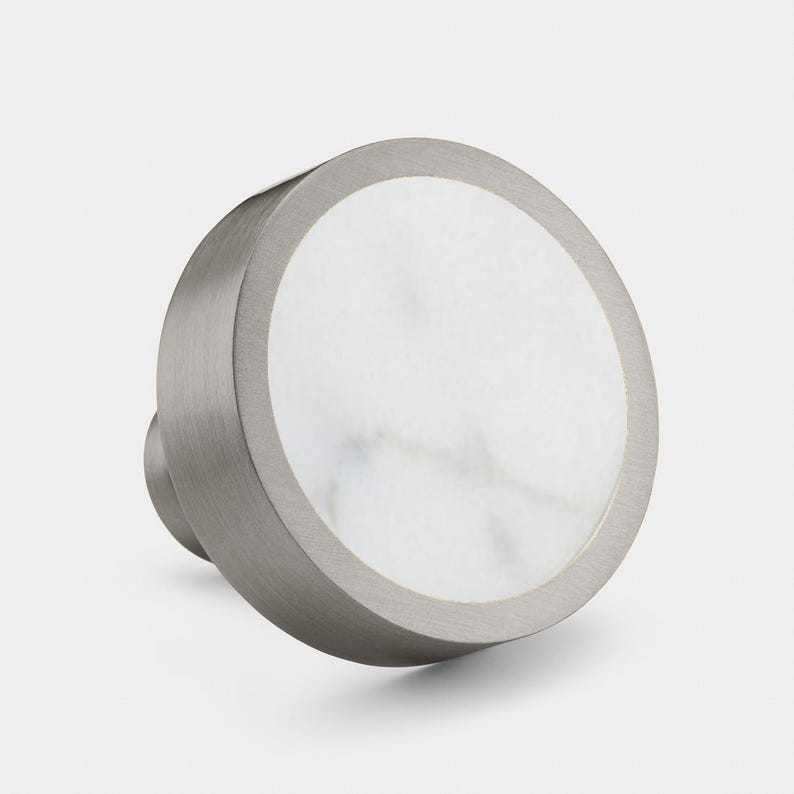 May include: A round, silver knob with a white marble inlay. The knob has a smooth, brushed finish.