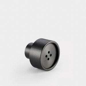 May include: A black metal cabinet knob with a round, slightly raised face and five small holes.