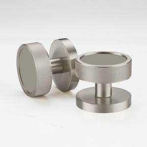 Może przedstawiać: Trzy gałki do szafek ze szczotkowanego niklu. Każda gałka ma okrągły kształt z żebrowanym brzegiem i płaskim, okrągłym środkiem. Gałki są przeznaczone do łatwego montażu i dodają nowoczesnego charakteru każdej szafce lub szufladzie.