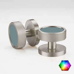 May include: Three brushed nickel cabinet knobs with a teal centre. The knobs have a cylindrical design with a ridged edge and a circular base. The knobs are displayed on a white background.