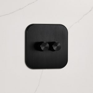 May include: Black dimmer switch with two round knobs. The switch is made of brushed metal and has a modern design.