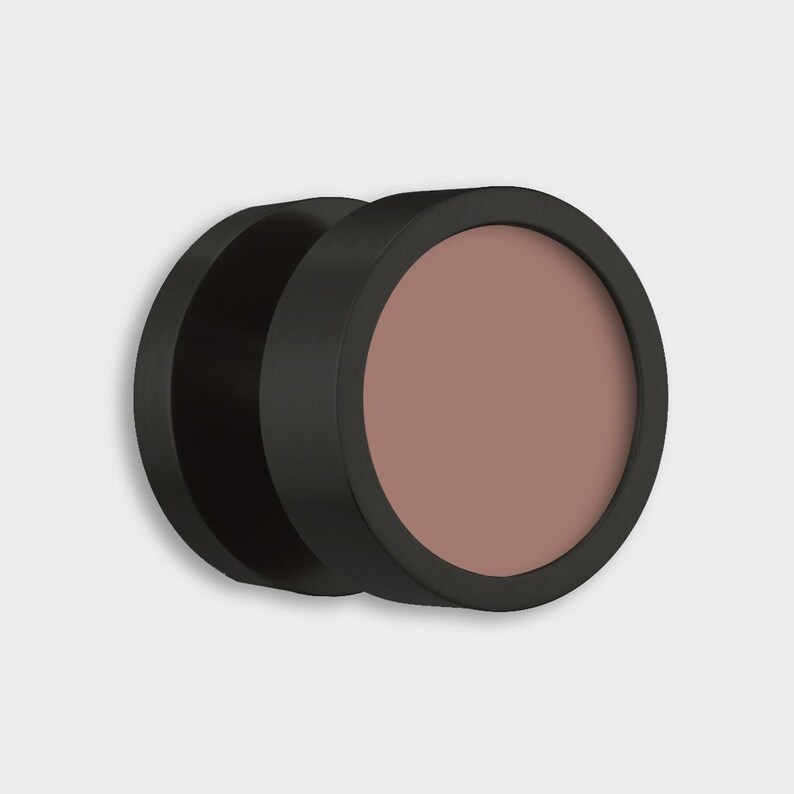 May include: A pair of black, circular cosmetic compacts. One compact is open, revealing a muted rose-colored powder. The compacts have a matte finish and are set against a plain white background.