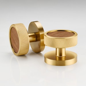 Może przedstawiać: Dwa złote gałki do szafek z drewnianym wkładką. Gałki mają fakturowany, okrągły wzór.