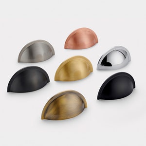 Può includere: Un set di sette pomelli per armadi in diverse finiture, tra cui nichel lucido, nero, rame, ottone e cromo. I pomelli hanno tutti la stessa forma, un design arrotondato leggermente curvo.