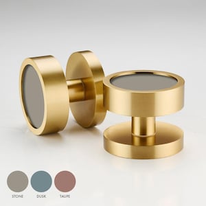May include: Two gold door knobs with a round, recessed centre. The knobs have a brushed finish and are available in three colours: stone, dusk, and taupe.