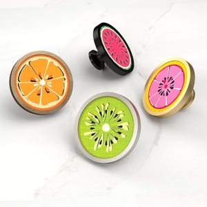 May include: Four cabinet knobs with fruit slice designs. The knobs feature an orange slice, a watermelon slice, a kiwi slice, and a pink grapefruit slice. The knobs have a variety of colours, including orange, green, pink, black, and gold.
