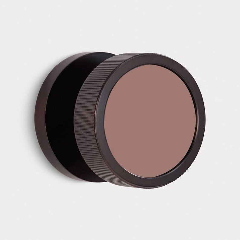 Puede incluir: Un espejo de pared redondo, marr&oacute;n oscuro, con un marco exterior estriado y una superficie de espejo de color rosa apagado. El espejo est&aacute; montado sobre un respaldo marr&oacute;n oscuro, creando un efecto de capas. Dise&ntilde;o minimalista y moderno.