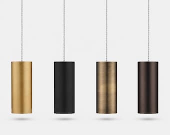 Op de afbeelding: Vier cilindervormige hanglampen die aan dunne, lichtgekleurde koorden hangen. De armaturen hebben verschillende afwerkingen: geborsteld goud, matzwart, geborsteld brons en een donkerbruine metallic afwerking, elk met een glad oppervlak.
