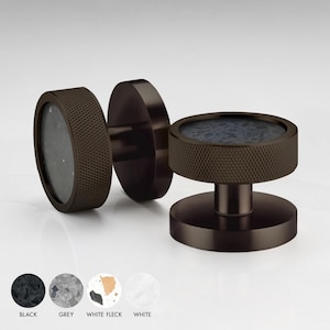 May include: Two round, dark brown cabinet knobs with a textured, ridged surface. The knobs have a circular, inset, black and white speckled design.