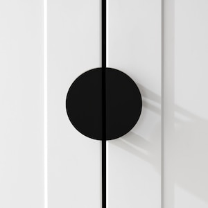 以下が含まれることがあります： 白いドアに取り付けられた、中央に縦の割れ目が入った黒い円形のドアノブ