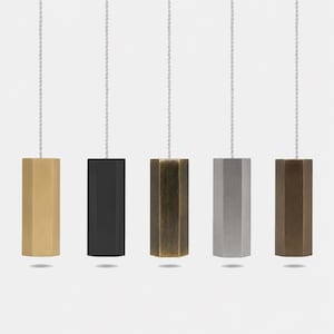May include: Five hexagonal light pull handles hanging from white braided cords. The pulls feature distinct finishes including brushed brass, matte black, antique bronze, brushed silver, and a dark metallic bronze, each with a smooth, geometric shape.
