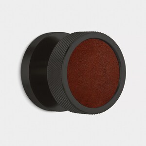 Peut inclure: Objet circulaire noir avec une bordure textur&eacute;e et un centre en cuir marron. L'objet pr&eacute;sente un design en couches, avec un disque noir lisse &agrave; gauche et une bande gris fonc&eacute; textur&eacute;e au milieu.