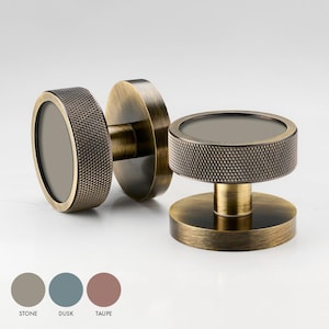 May include: Two antique brass cabinet knobs with a textured, circular design. The knobs have a round, flat base and a raised, circular top with a recessed centre.